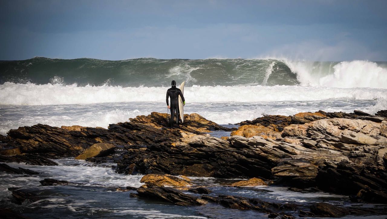 Surfer on rocks looking at the waves